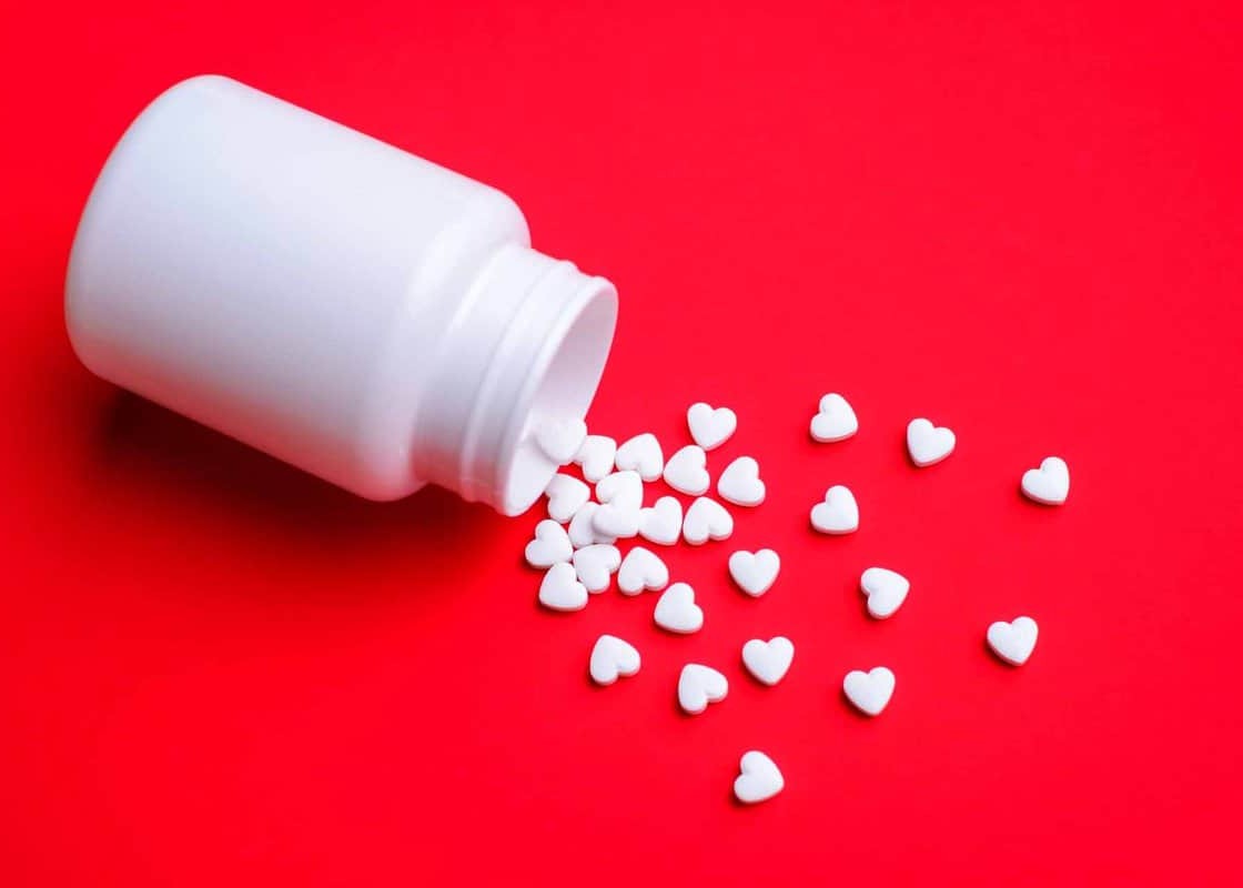 Small white love pills with a plastic bottle on red colorful table. Concept of love pills, potency, loneliness, heart disease.