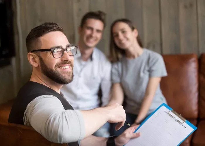 Smiling professional man psychologist consulting young couple, friendly psychotherapist or marriage counselor expert looking at camera counseling clients in office, family therapy concept, portrait