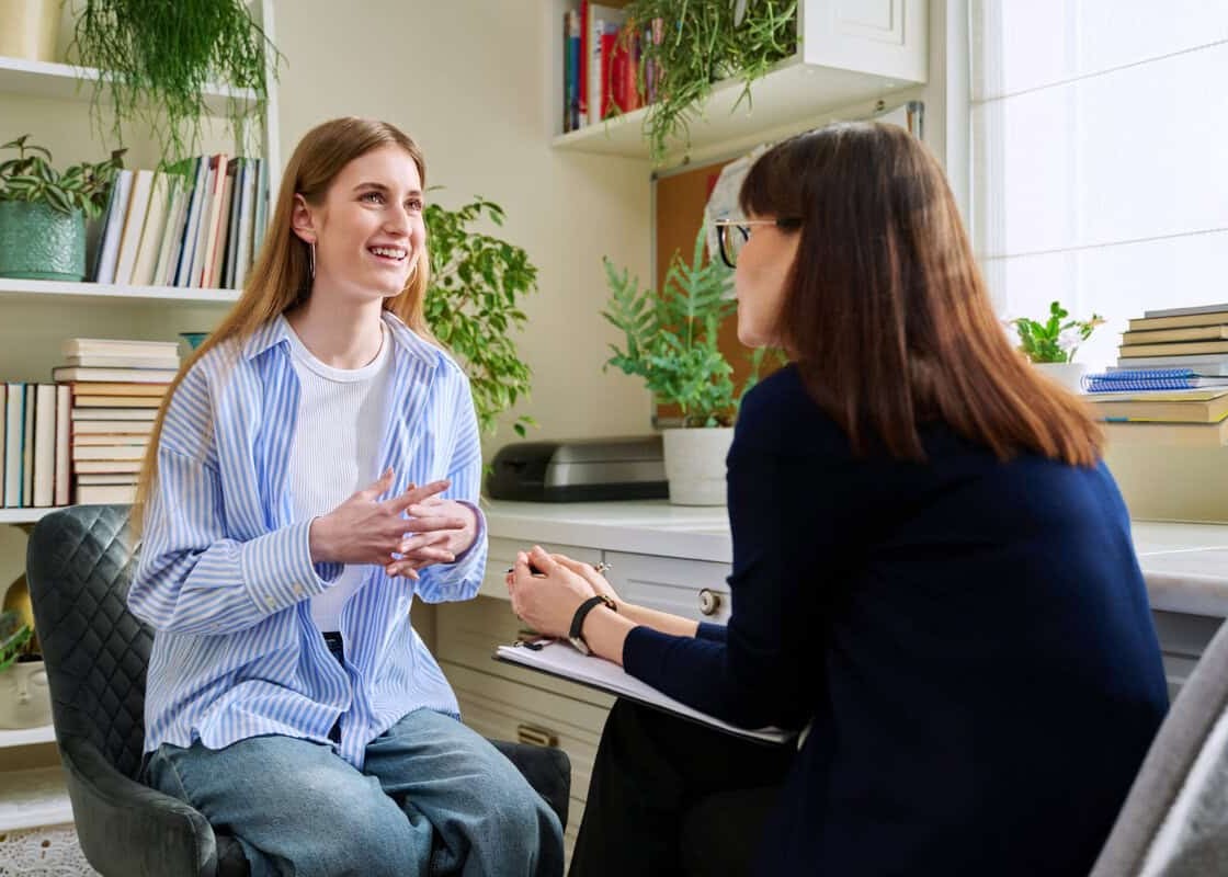 Smiling positive young teen female patient talking to professional mental therapist. Teenager girl high school college student in therapy with psychologist psychotherapist counselor. Treatment support
