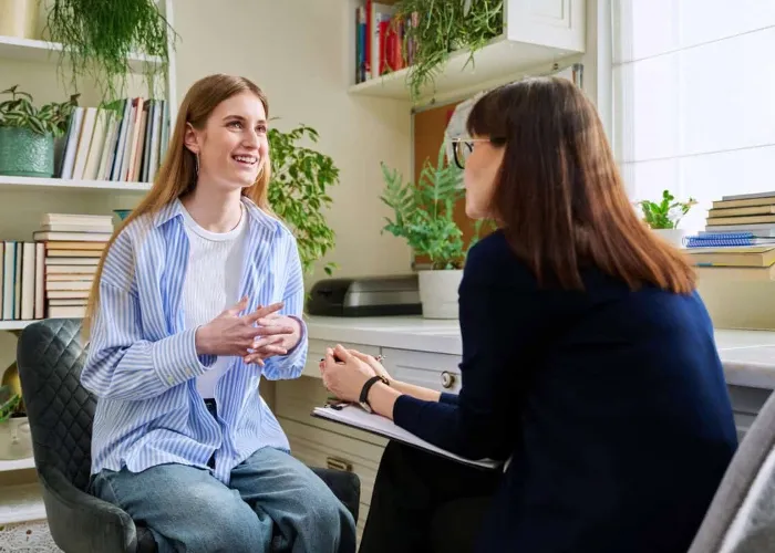 Smiling positive young teen female patient talking to professional mental therapist. Teenager girl high school college student in therapy with psychologist psychotherapist counselor. Treatment support