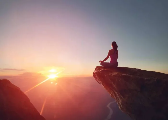 Woman practices yoga and meditates on the mountain.