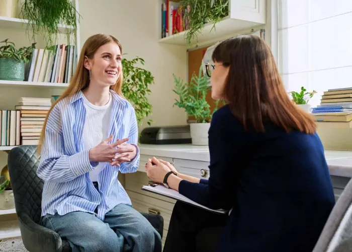 Smiling positive young teen female patient talking to professional mental therapist. Teenager girl high school college student in therapy with psychologist psychotherapist counselor. Treatment support