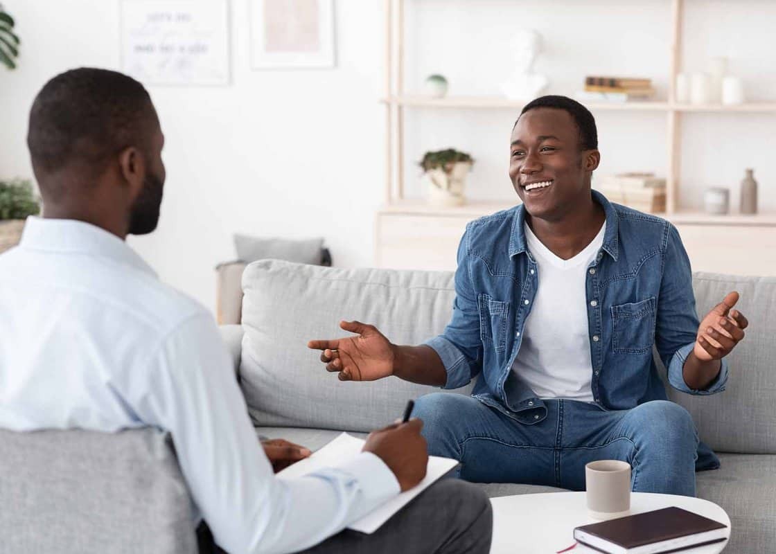 Successful Therapy. Cheerful black man talking to psychologist on meeting at his office, sharing his progress with doctor