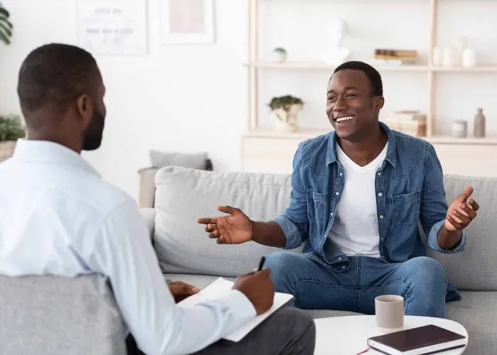 Successful Therapy. Cheerful black man talking to psychologist on meeting at his office, sharing his progress with doctor