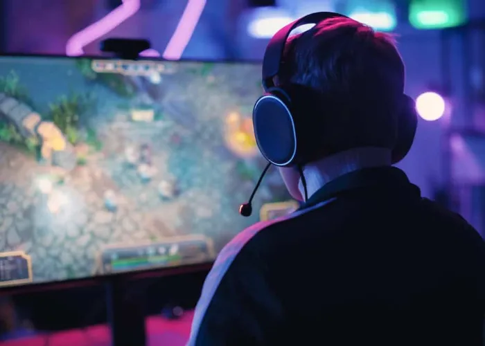 Over the Shoulder Angle of a Young Female Gamer Winning in a Video Game on Personal Computer in a Neon Lit Living Room at Home. Cozy Evening at Home in Loft Apartment.