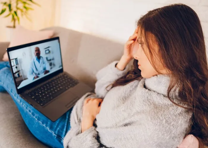 Young beautiful woman having video call with doctor using laptop at home