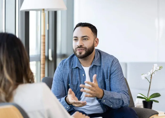 A young male therapy patient gestures as he talks about something with a female therapist.