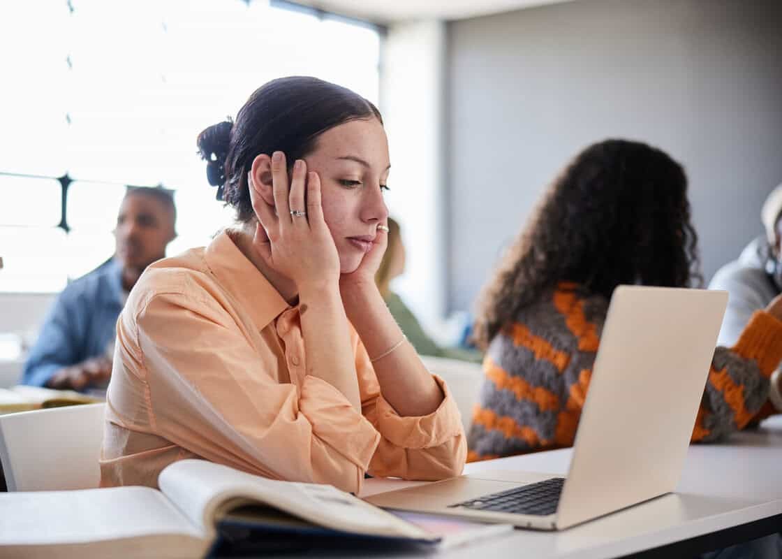 Young female college student sitting at a table and looking distracted during a lesson in a classroom at school