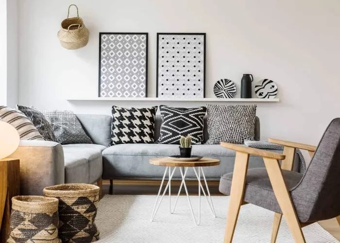 Real photo of a small table standing between a sofa with pillows and an armchair on a white rug in boho living room interior with posters on a shelf