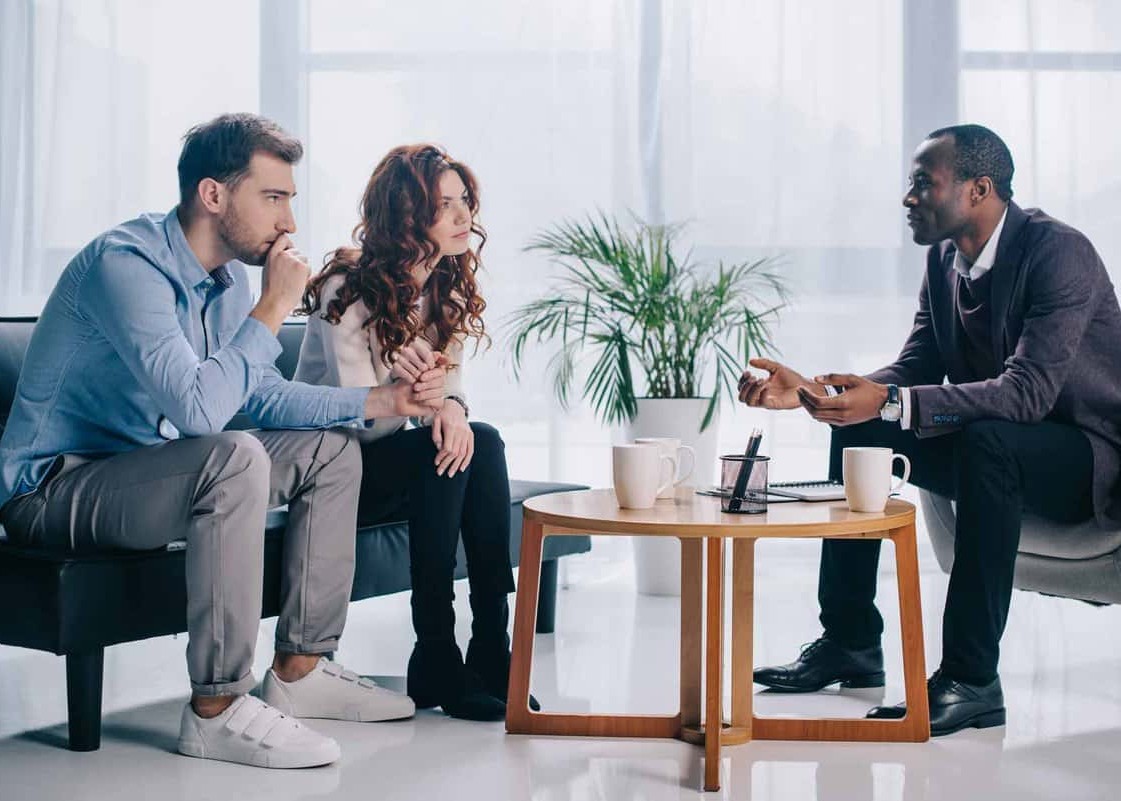 Smiling african american psychiatrist talking to young couple in office