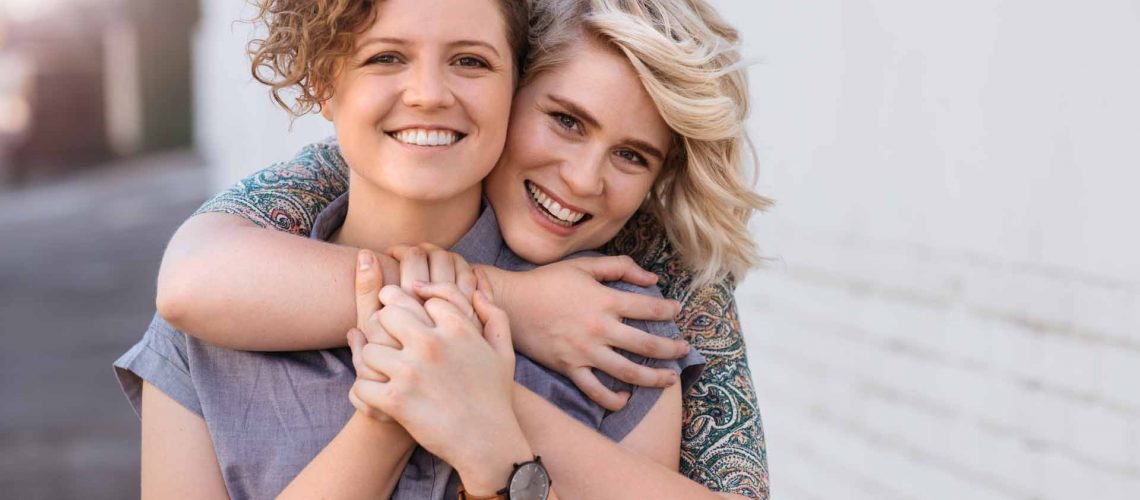 Portrait of a smiling young lesbian couple hugging each other while standing together on a city street
