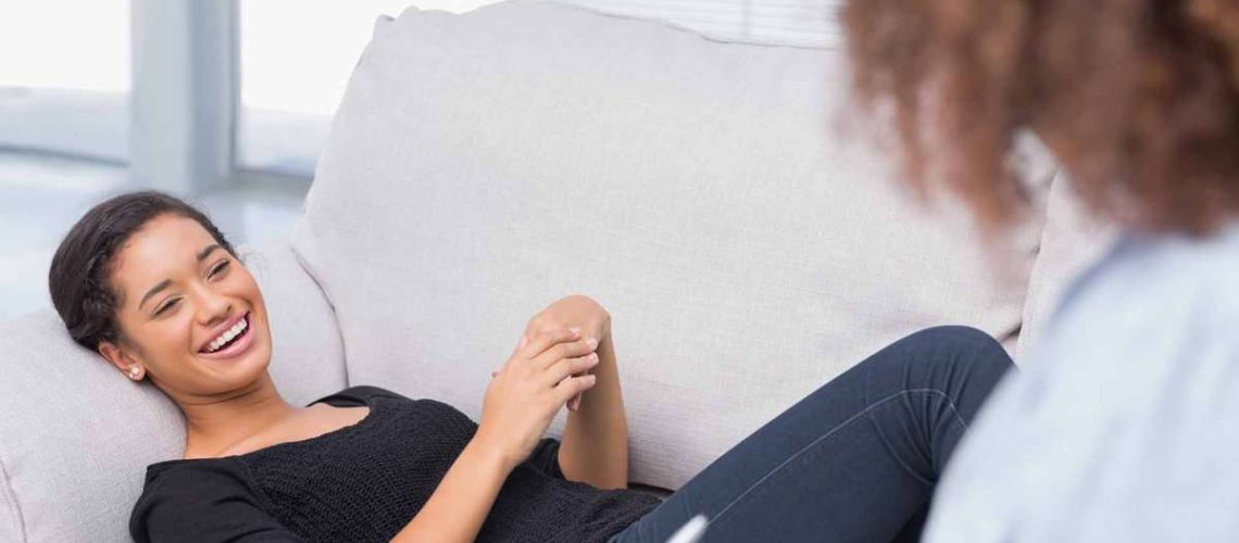 Woman lying on therapists couch looking happy as therapist is writing