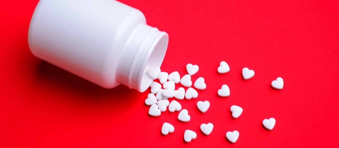 Small white love pills with a plastic bottle on red colorful table. Concept of love pills, potency, loneliness, heart disease.